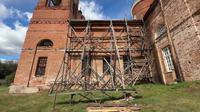 A brick church in the scaffolding: restoration of an ancient building under a bright sky.