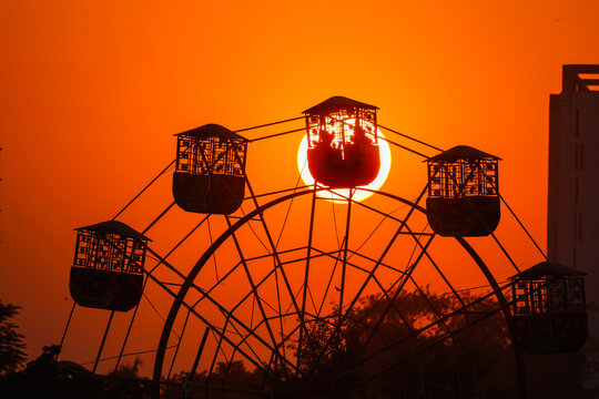 View of a Ferris wheel silhouetted against a vibrant orange sunset in Dhaka, Dhaka Division, Bangladesh.
