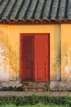 Traditional louvered wooden entrance doors and clay tile roof eaves on weathered ochre stucco facade of ancient oriental building