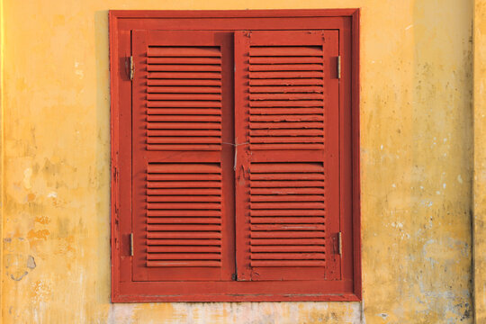 Traditional red louvered window shutters on ochre yellow stucco wall, minimalist architecture texture and horizontal graphic backdrop