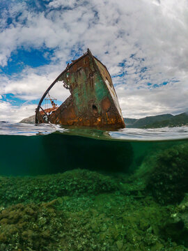 View of a rusted shipwreck partially submerged in clear water with a mountainous coastline in the background in Rose, Opstina Herceg Novi, Montenegro.
