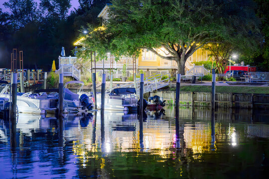Boats docked at a small marina near an illuminated waterfront building along the Conway Riverwalk at blue hour twilight in Conway, South Carolina.