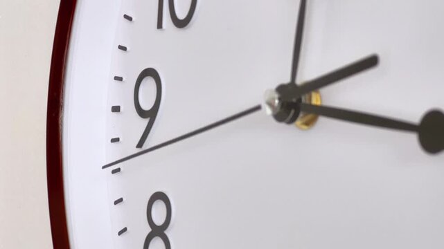 Close-up shot of a classic round wall clock face with black numbers and hands ticking away, illustrating the concept of time passing, deadlines, and schedule.
