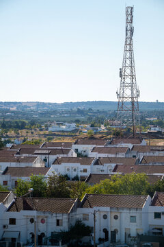 View of a tall telecommunications tower rising above a residential area with white houses and terracotta roofs in Elvas, Portalegre District, Portugal.