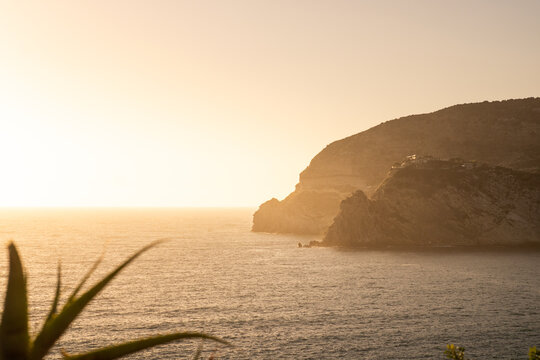 View of the rocky coastline of Ischia island at sunset with calm sea and golden light in Ischia, Campania, Italy.