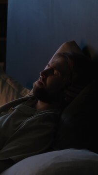 Vertical shot of Caucasian young adult man sleeping in bed and yawning during night rest. Footage suitable for healthcare campaigns, insomnia treatments, and wellness apps