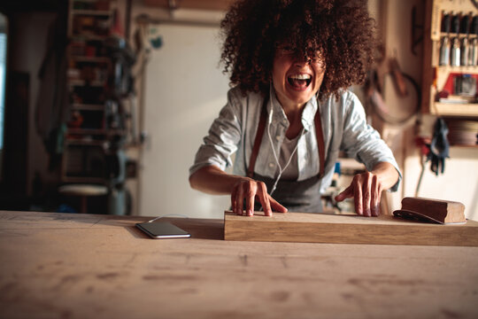 Smiling woman sanding wood plank in home carpentry workshop