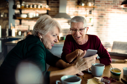 Two senior women using smartphone at home kitchen
