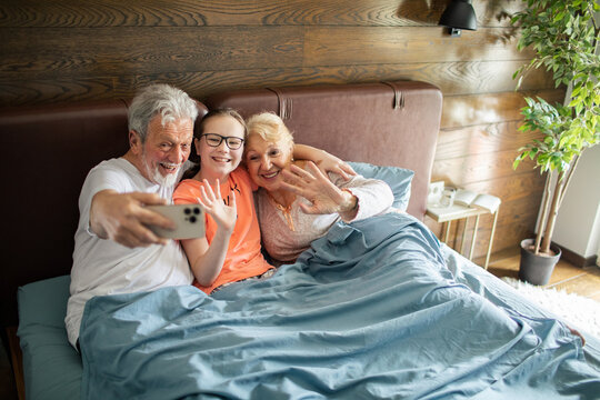Grandparents and granddaughter taking selfie in bed at home