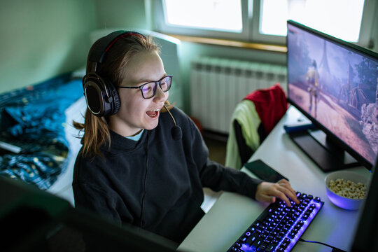 Teen girl gamer wearing headset playing pc at home