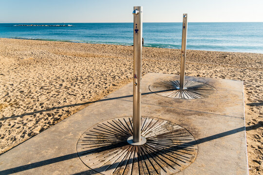 View of stainless steel beach showers on a concrete platform on a sandy beach with the Mediterranean Sea in the background in Barcelona, Catalonia, Spain.