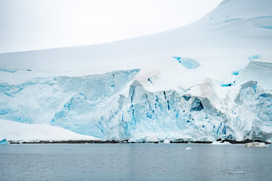 View of the massive, jagged blue glacial ice formations rising above the cold waters of the Antarctic coastline. Antarctica.
