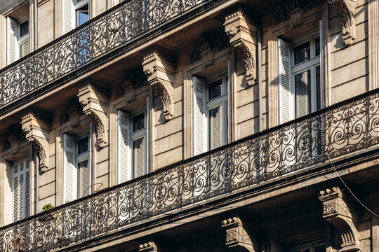 Historic limestone building facade with ornate wrought iron balconies and tall shuttered windows in central Bordeaux, France.