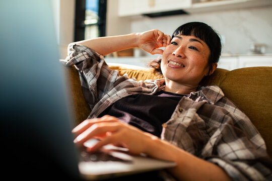 Smiling woman relaxing on sofa with laptop at home