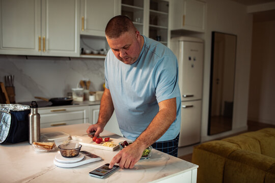 Man tracking calories while prepping healthy lunch at home kitchen