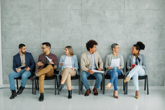 Portarit of a group of young business people using mobile phones waiting to apply for a job in the office