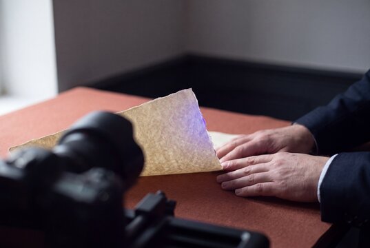 Historian or archivist carefully handling an antique parchment manuscript during digitization and photography