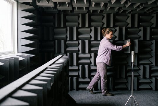 Female sound engineer adjusting acoustic foam wedges inside a professional anechoic chamber with microphone
