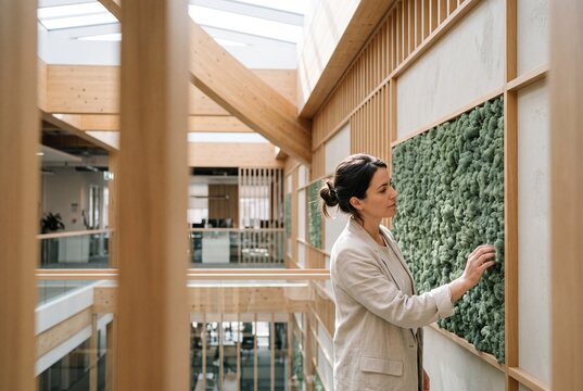 Young businesswoman touching a preserved moss wall in a modern sustainable eco-friendly timber office