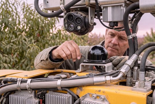 Technician Adjusting Sensor System on Autonomous Agricultural Robot in an Orchard