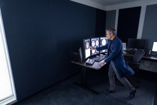 Male radiologist analyzing brain MRI scans on multiple diagnostic computer monitors in hospital office
