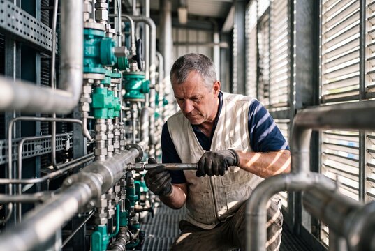 Middle-aged industrial technician repairing metal pipe system with a wrench in a factory facility
