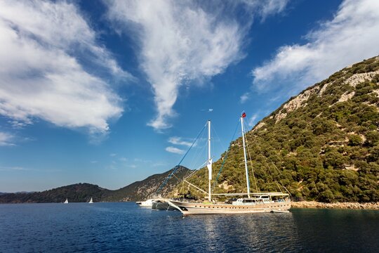 View of a traditional wooden gulet boat anchored in a calm blue bay surrounded by lush green hills under a bright sky in Fethiye, Mugla, Turkey.
