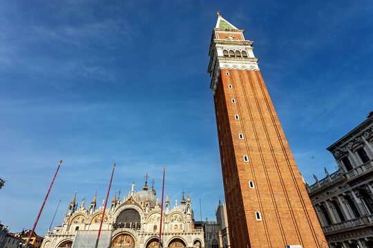 View of St. Mark's Campanile towering over the ornate facade of St. Mark's Basilica under a clear blue sky in Venice, Veneto, Italy.