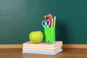 Books, notebooks, apple and stationery on wooden table against chalkboard. Space for text © New Africa