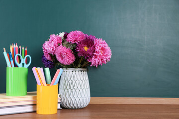 Stack of books, stationery and bouquet on wooden table against chalkboard. Space for text © New Africa