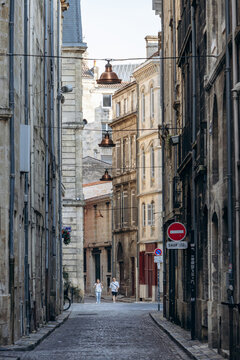 Bordeaux, France - July 14, 2026: Pedestrians walk along a narrow cobblestone street lined with historic stone buildings in the old town