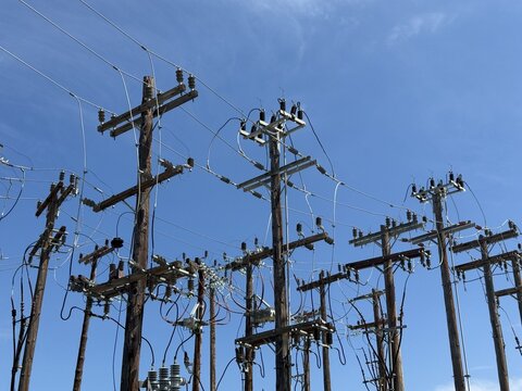 View of wooden utility poles with complex electrical wiring and insulators against a clear blue sky in Skiathos, Greece.