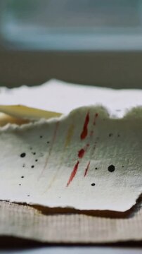 Vertical video: Lifting torn watercolor sheet from stack on linen tabletop near window