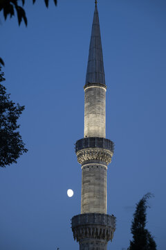 View of a slender stone minaret illuminated against a deep blue evening sky with a visible moon in Istanbul, Istanbul, Turkiye.
