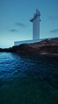 Modern lighthouse rocky shore sea bay background. This scenic commercial background captures a contemporary white lighthouse standing on a rugged coastline overlooking clear blue water and a serene se