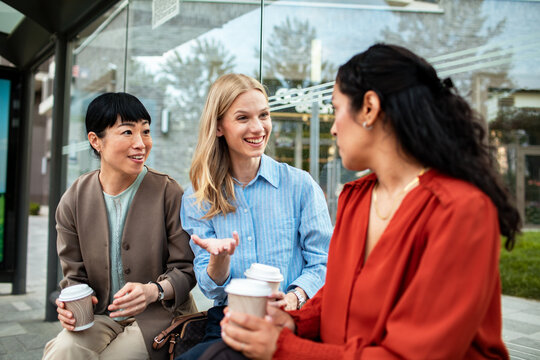 Three women chatting over coffee at a bus stop