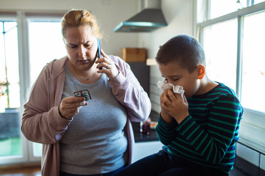 Concerned mother calling doctor for sick son in home kitchen