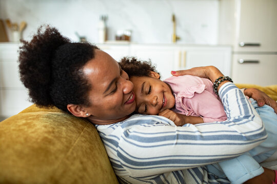 Mother cuddling daughter on cozy sofa at home