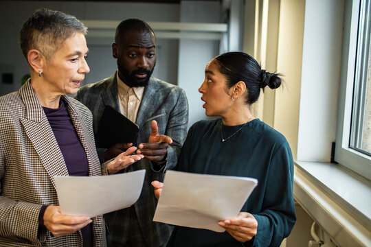 Three coworkers debating paperwork by office window