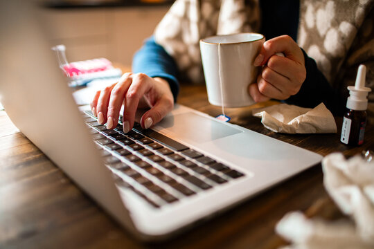 Sick person working on laptop at home with tea