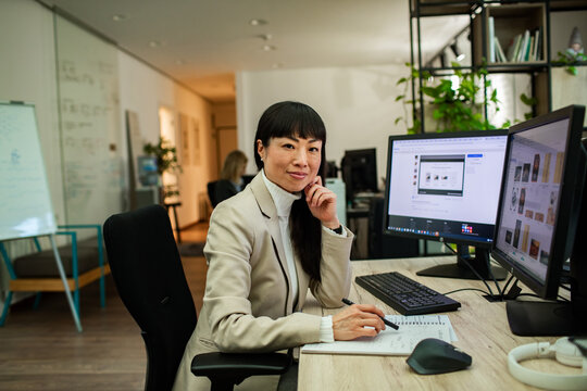Confident businesswoman working at dual monitors in modern office