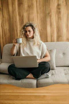 Woman working remotely on laptop drinking coffee on sofa