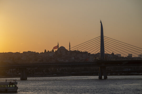 View of the Halic Metro Bridge silhouetted against the sunset with a mosque and minarets in the background over the Golden Horn in Istanbul, Istanbul, Turkiye.