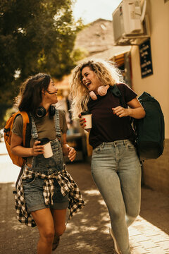Two young female friends laughing walking on city street