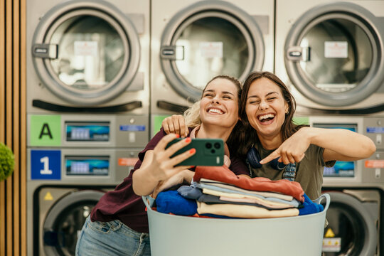 Happy young women taking selfie while doing laundry