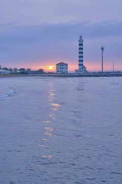 View of the Faro di Piave Vecchia lighthouse at sunset with its reflection on the calm Adriatic Sea in Lido di Jesolo, Veneto, Italy.