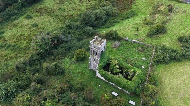 Aerial drone footage looking down over the historic Saint Patricks Church ruins, stone walls, overgrown vegetation and surrounding green pastureland in Toberrooaun, County Mayo, Ireland.