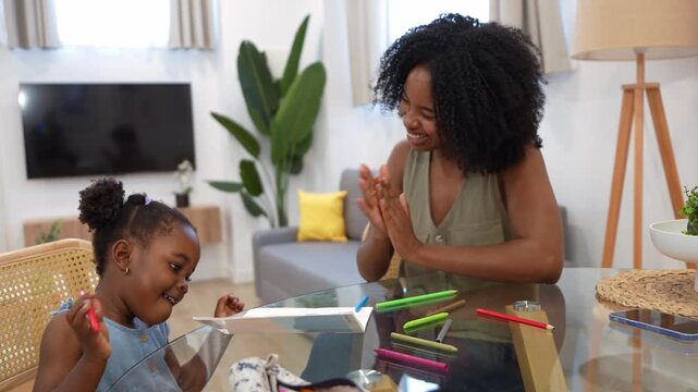 Happy african american mother and her little daughter drawing with colorful markers at home, sharing a high five and a loving moment