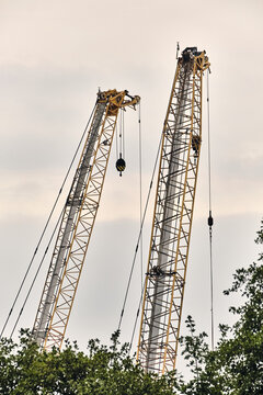 Taulov, Denmark - 28 August 2026: View of two tall yellow construction cranes at the Google Data Center extension building site, rising above green trees against a cloudy sky.