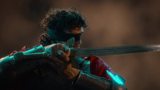 Side shot of blindfolded young adult Caucasian man wearing knight armor raising broadsword in combat stance. Clip suitable for fantasy game marketing and historical film storytelling